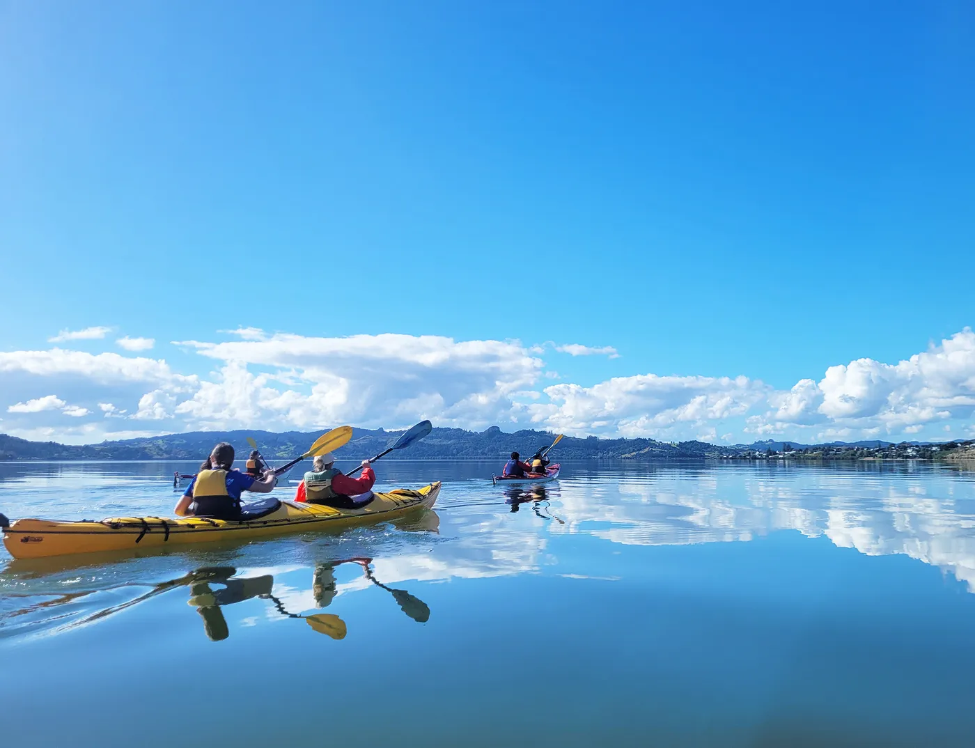 A small group paddling sea kayaks across mirror-calm water under a wide blue sky